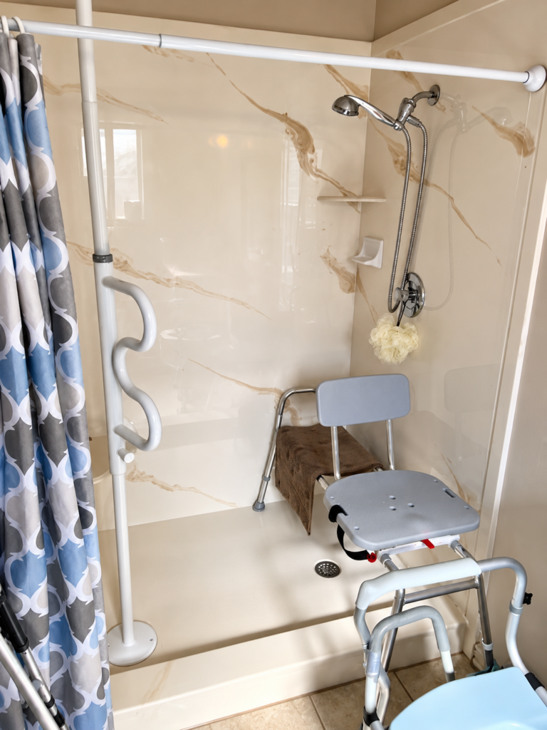 Accessible bathroom featuring a raised toilet seat with safety armrests, a shower chair, and other bathroom safety aids for seniors.