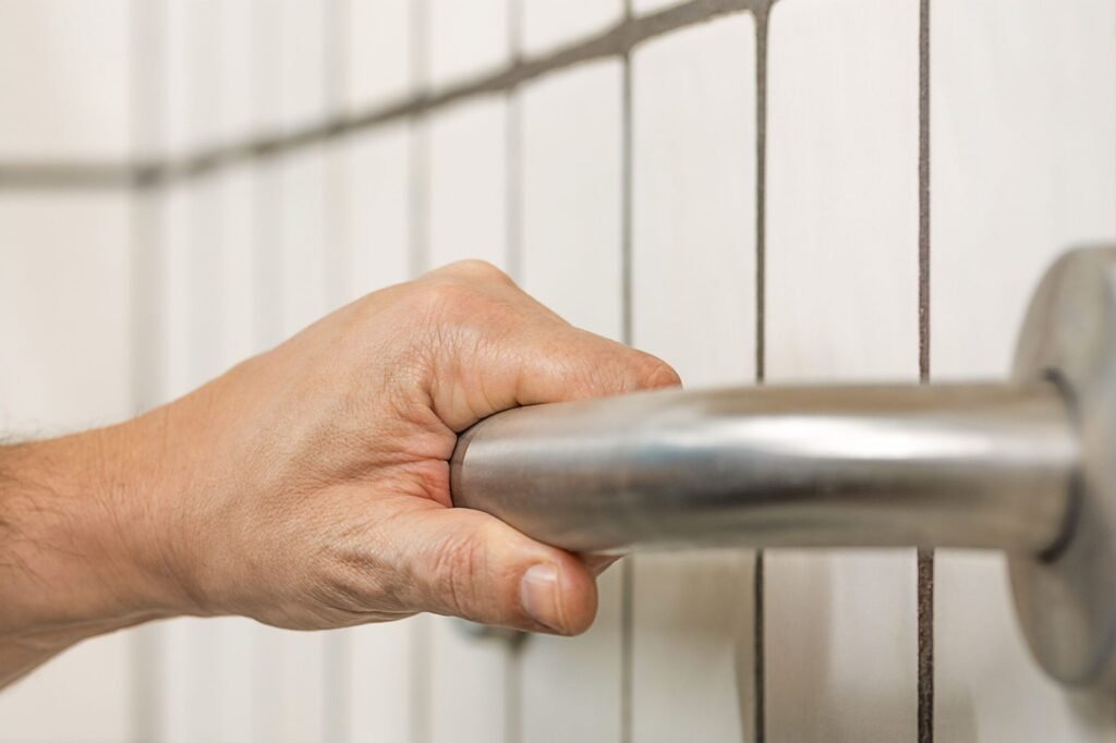 Daily Living Aids for Independence-Hand gripping a stainless steel bathroom grab bar mounted on a tiled wall for balance and fall prevention.