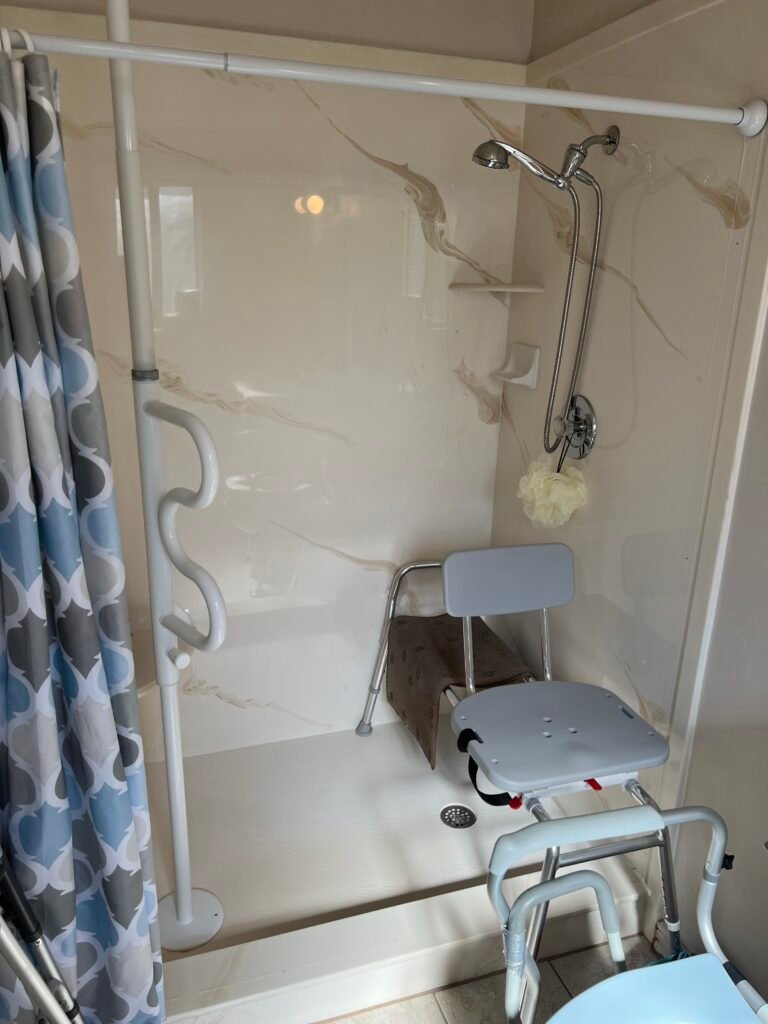 Dad's walk-in shower equipped with a shower chair, a floor-to-ceiling grab pole, and a wall-mounted grab bar. These bathroom safety aids helped him sit, stand, and shower more safely while maintaining his independence at home.