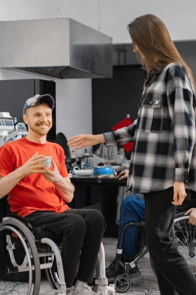 gentleman sitting in a wheelchair enjoying a drink laughing with a friend