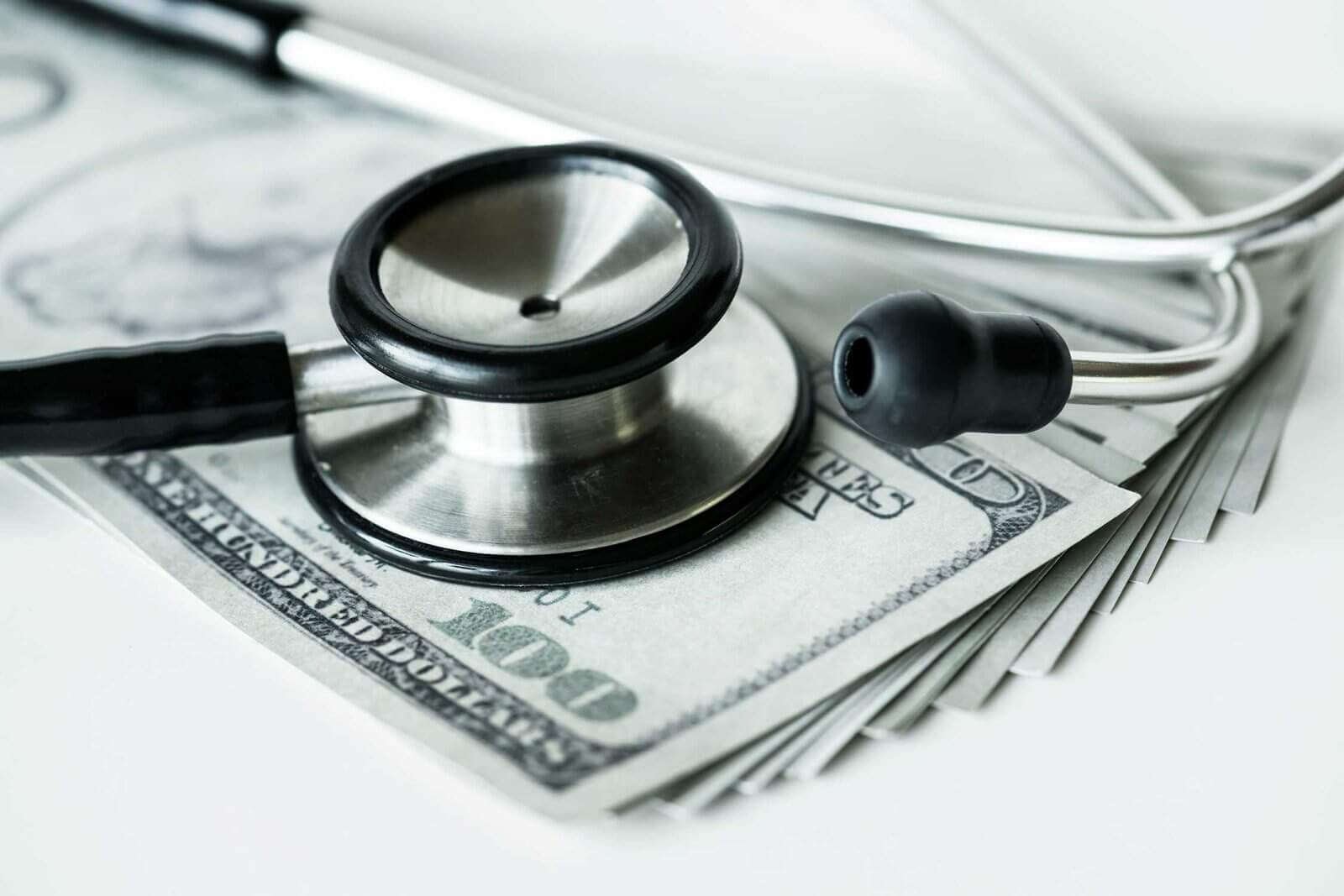 Medical stethoscope on dollar bills highlighting healthcare cost concerns.