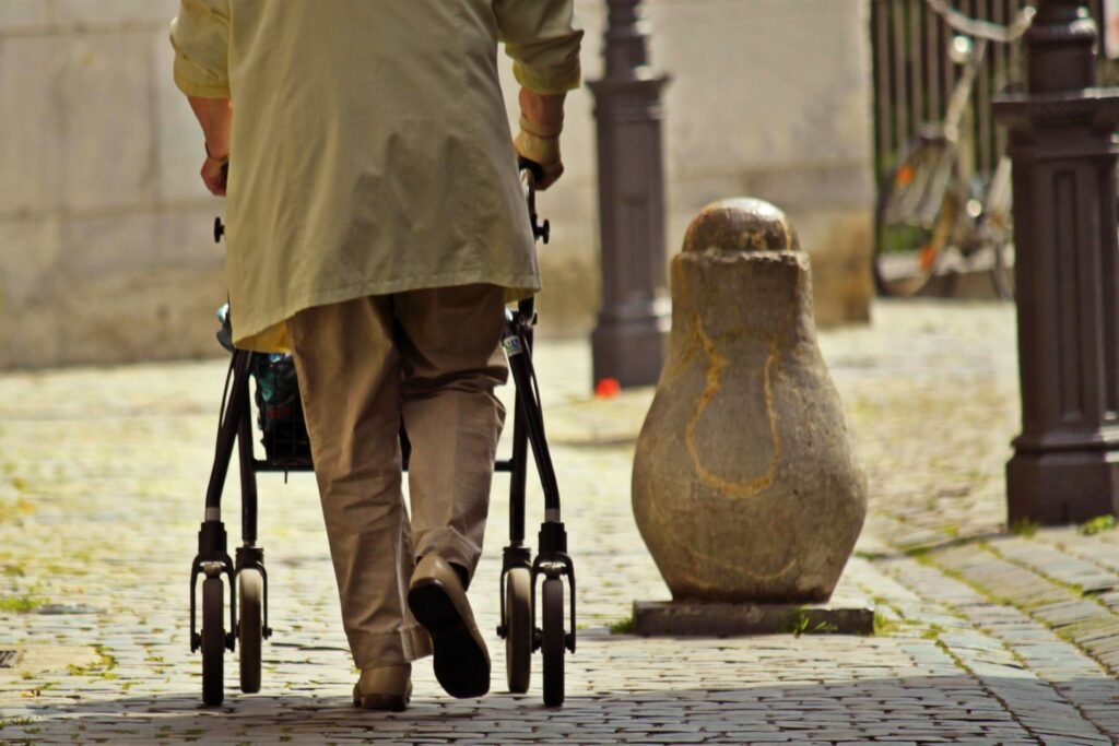 Senior walking outdoors with a four-wheel rollator walker on a cobblestone street, demonstrating safe mobility and independent walking.