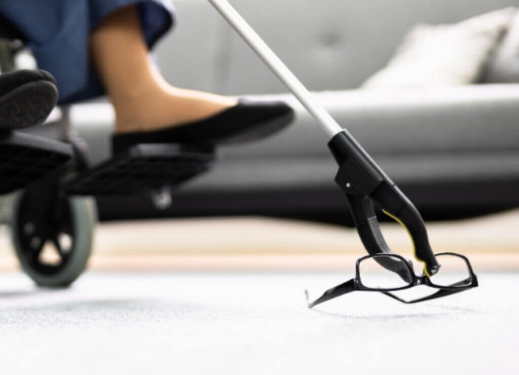 Someone using a grabber tool in a wheelchair picking up her glasses