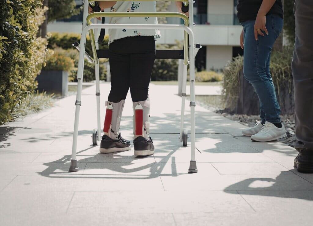 Person using a walker during rehabilitation while receiving support from caregivers outdoors