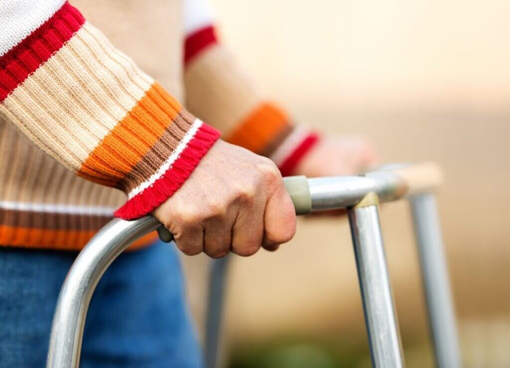 Close-up of a person's hand gripping a standard walker for support and stability