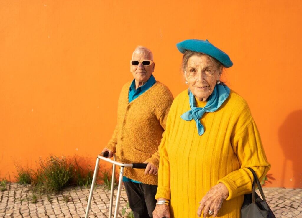 Stylish older couple outdoors, with one person using a walker while remaining active and independent.