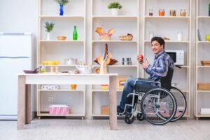 Wheelchair user preparing food independently in an accessible kitchen with open shelving and easy-to-reach work surfaces.