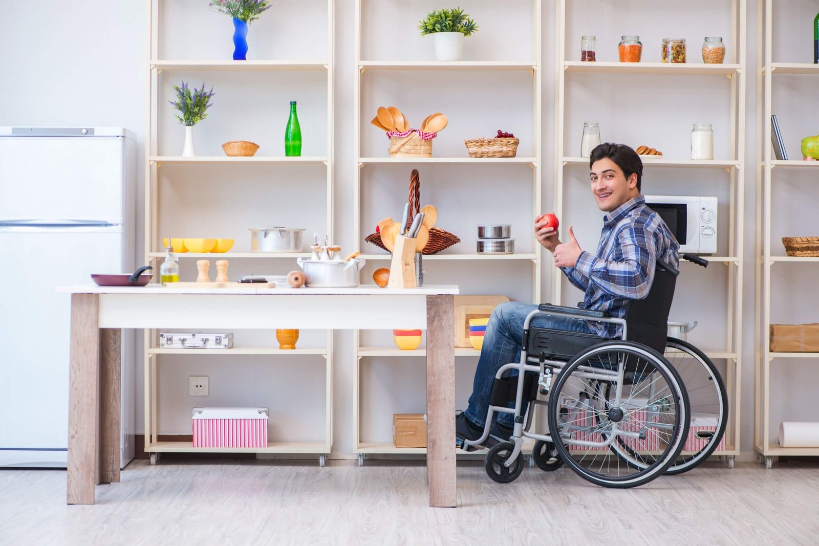 Wheelchair user preparing food independently in an accessible kitchen with open shelving and easy-to-reach work surfaces.