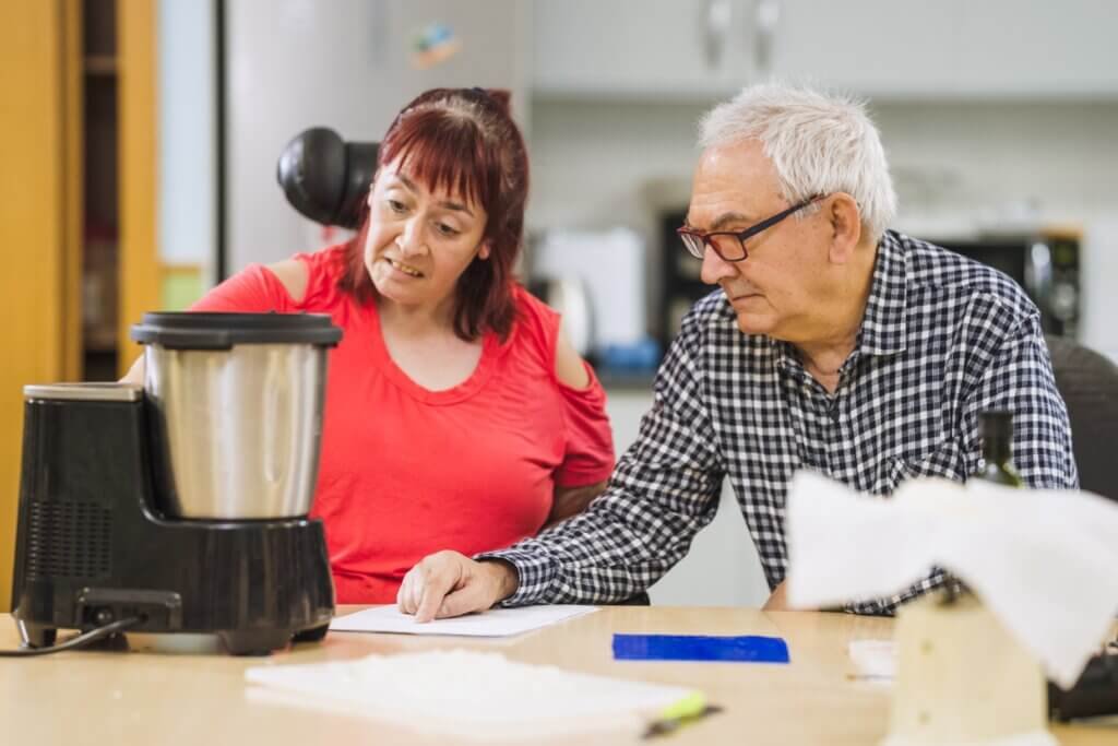 Adult with a disability using an adaptive kitchen appliance with caregiver support during meal preparation.