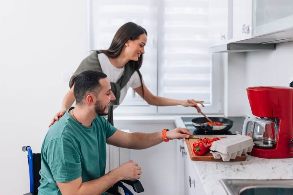 Wheelchair user preparing a meal in an accessible kitchen with caregiver assistance and adaptive cooking techniques.