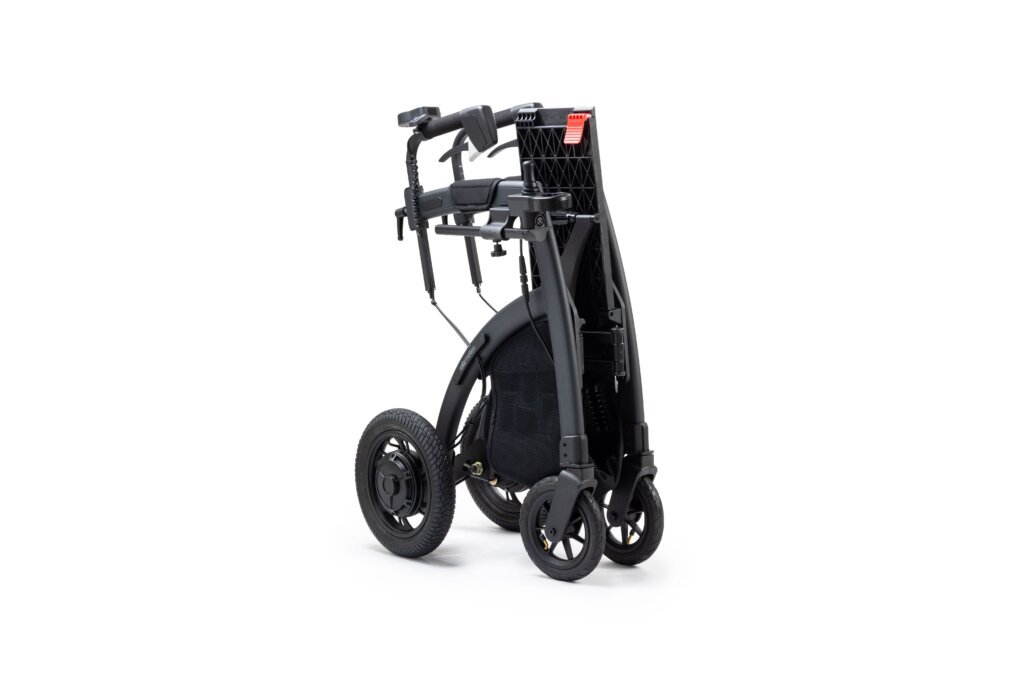 Black folding rollator walker with four wheels, padded seat, backrest, hand brakes, and storage bag, collapsed for transport and storage on a light gray background.