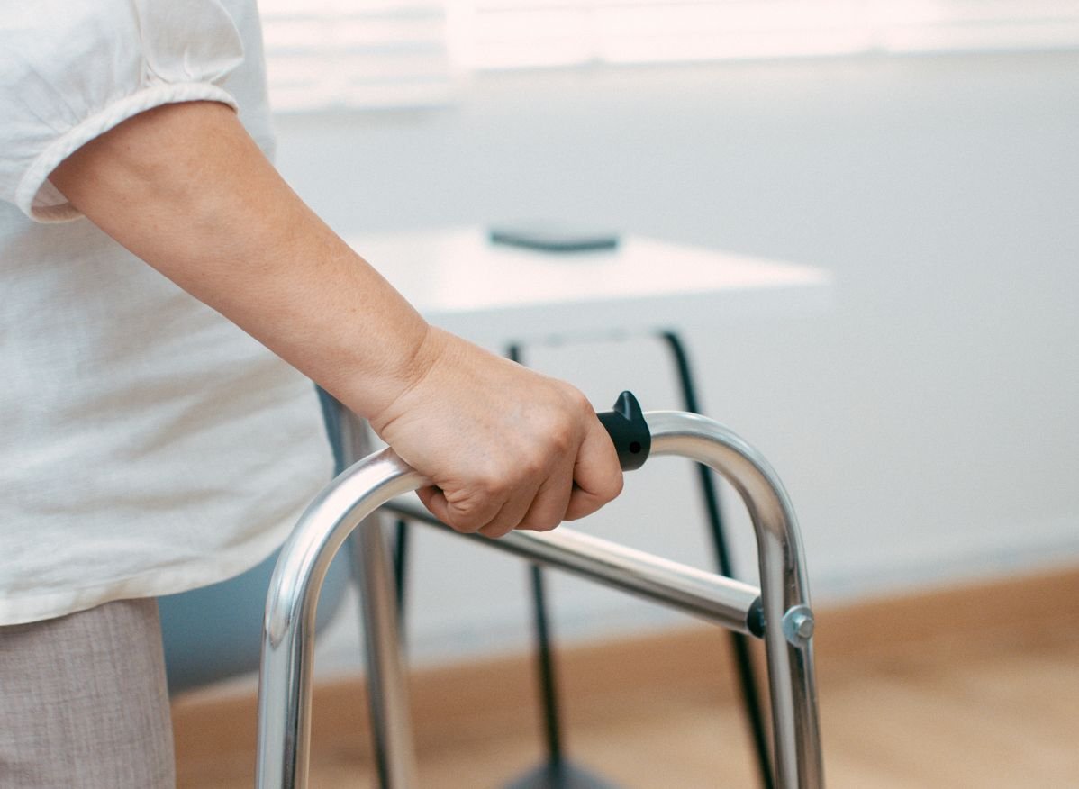 Close-up of a person gripping the handle of a standard walker for balance and mobility support.