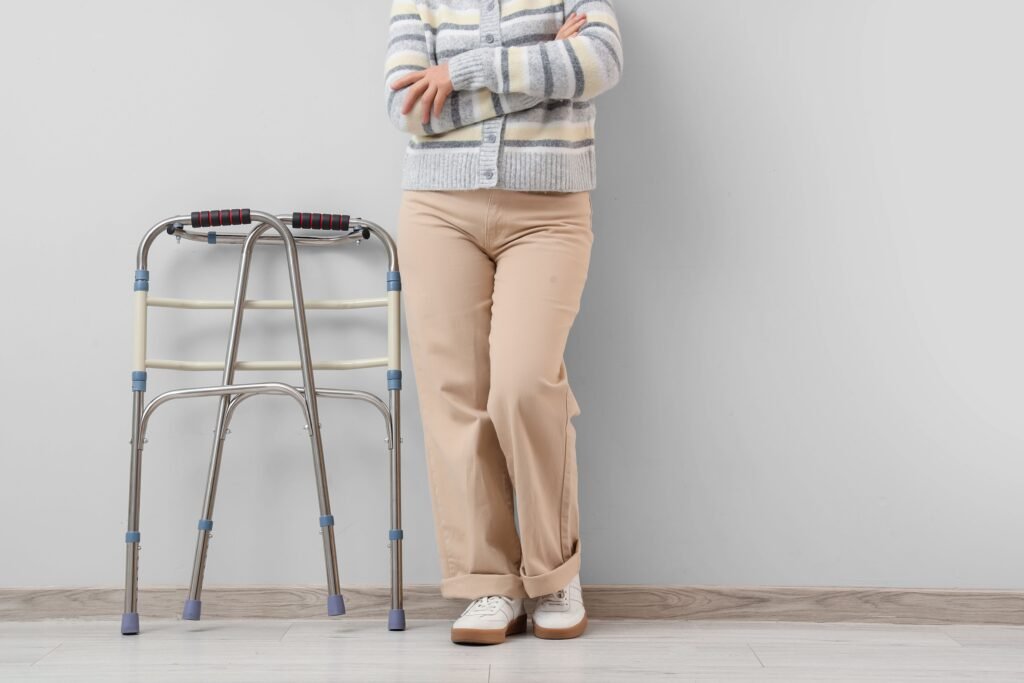 Person standing beside a standard folding walker with padded hand grips in a home setting, illustrating mobility support for walking assistance.