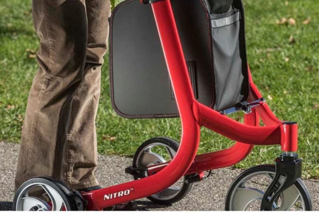 Front angled view of a red 3-wheel walker with ergonomic handles, removable storage bag, storage tray, and large maneuverable wheels for everyday mobility support.