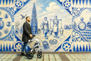 A man using a four-wheel rollator walks past a large blue-and-white Delft-style mural, symbolizing confidence, mobility, and independence in a bright urban setting.