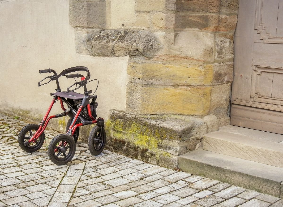 Red rollator walker parked outside a stone building near a doorway and step entrance.